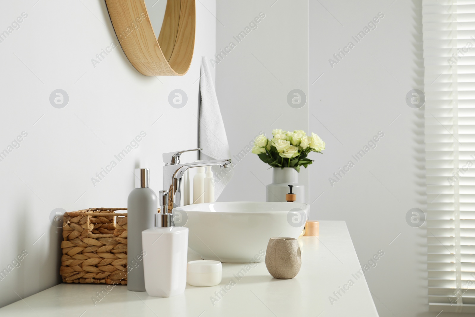 Photo of Vase with beautiful white roses and toiletries near sink in bathroom