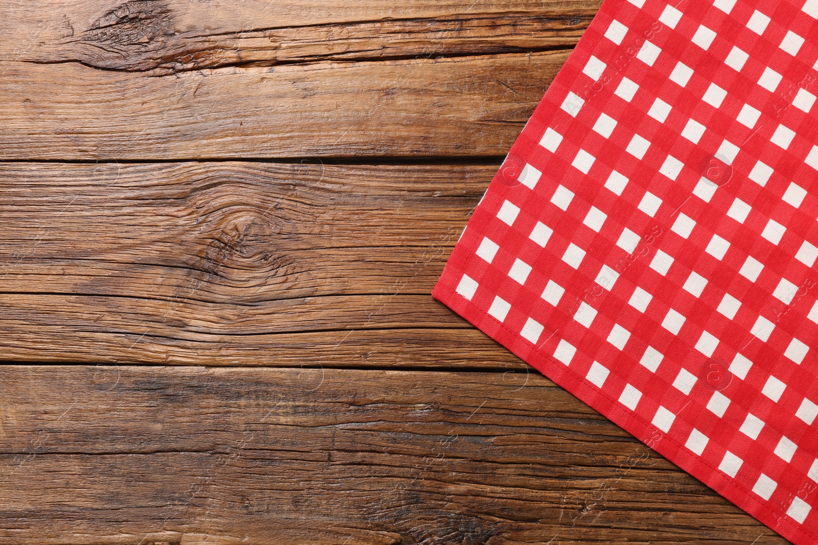 Photo of Red checkered tablecloth on wooden table, top view. Space for text