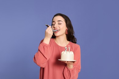 Photo of Coming of age party - 21st birthday. Smiling woman tasting delicious cake with number shaped candles on violet background
