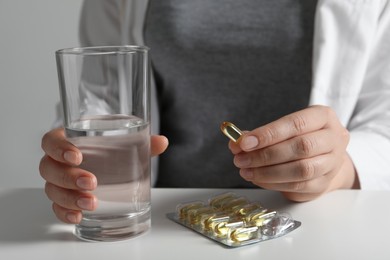 Photo of Woman with glass of water and pill at white table, closeup