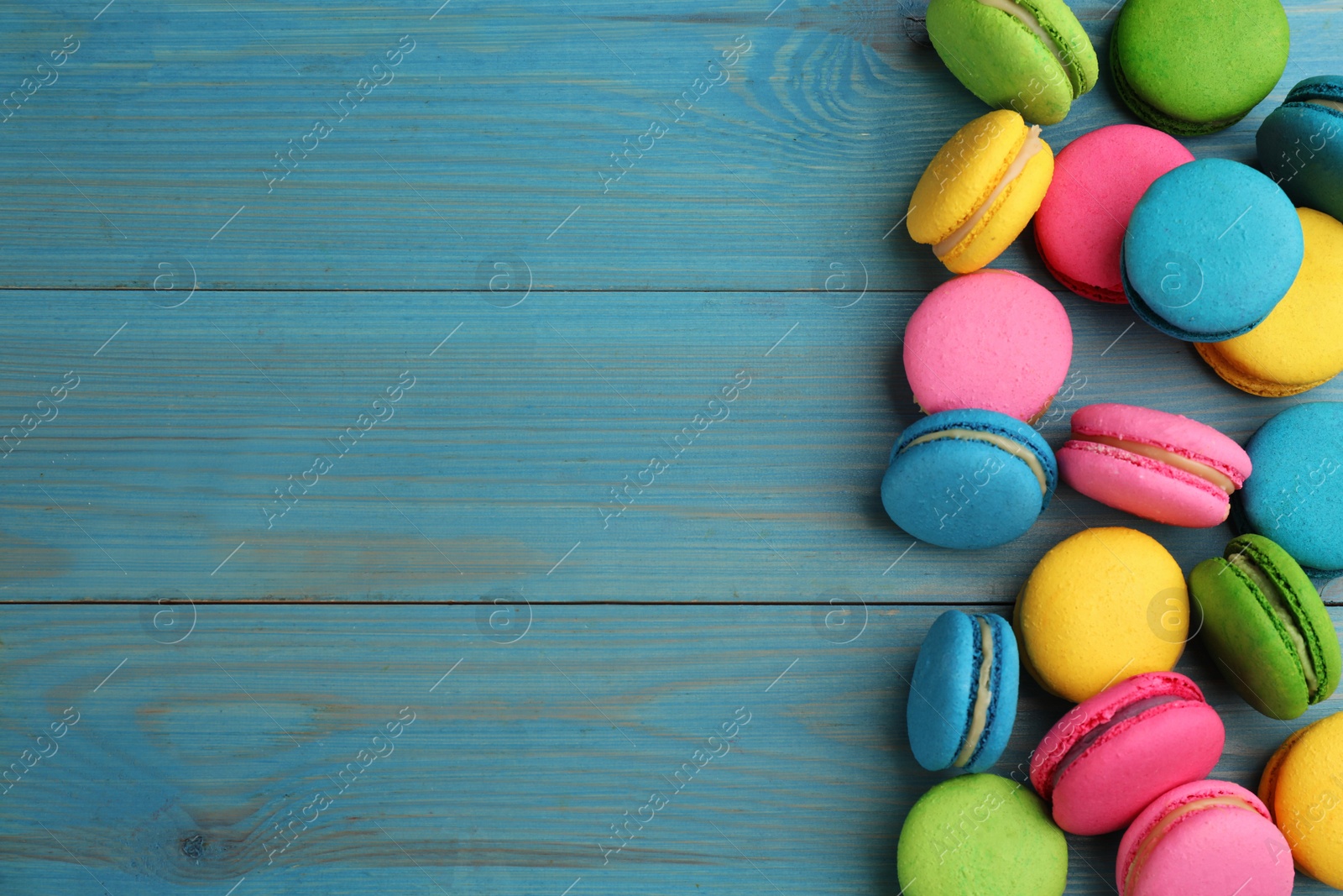 Photo of Delicious colorful macarons on light blue wooden table, flat lay. Space for text