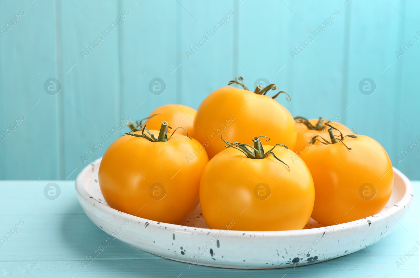 Photo of Ripe yellow tomatoes on light blue wooden table