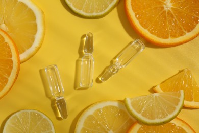 Photo of Skincare ampoules with vitamin C and citrus slices on yellow background, flat lay