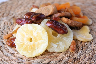 Photo of Pile of different tasty dried fruits on wicker mat, closeup
