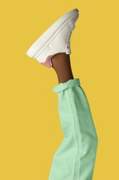 Photo of Woman wearing sneakers on yellow background, closeup