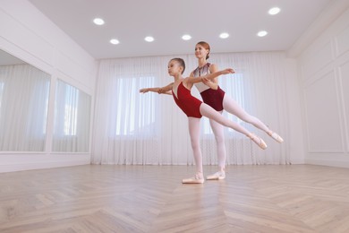 Photo of Little ballerina and her teacher practicing dance moves in studio. Space for text 
