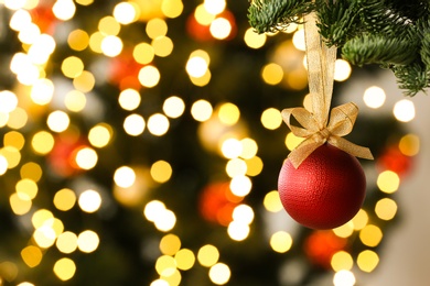 Beautiful Christmas ball hanging on fir tree branch against blurred lights, closeup. Space for text