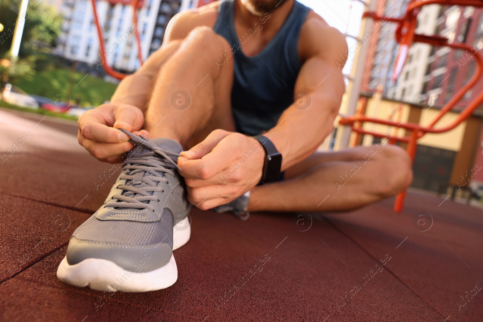 Photo of Man tying shoelaces before training at outdoor gym, closeup