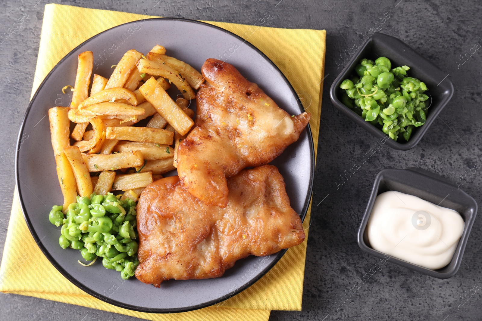 Photo of Tasty fish, chips, sauce and peas on grey table, flat lay