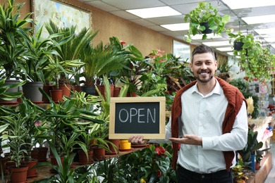 Male business owner holding OPEN sign in his flower shop