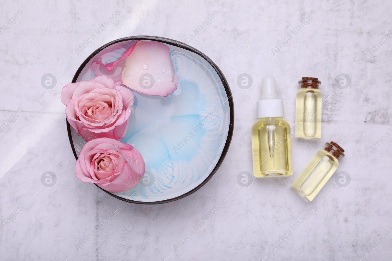 Photo of Flat lay composition with bowl of water, flowers and essential oils on light table. Spa treatment