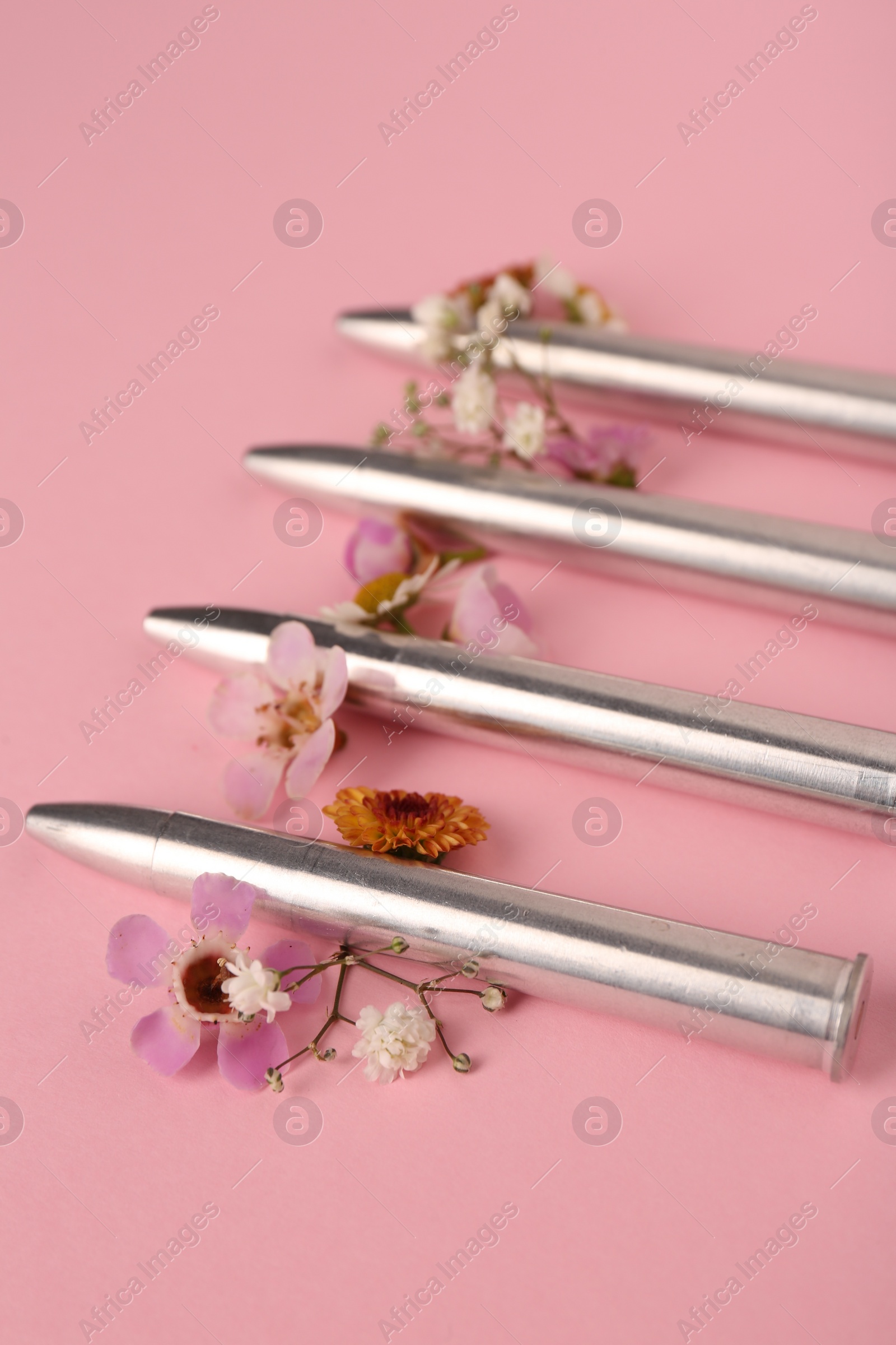 Photo of Metal bullets and beautiful flowers on pink background, closeup