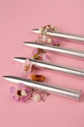 Photo of Metal bullets and beautiful flowers on pink background, closeup