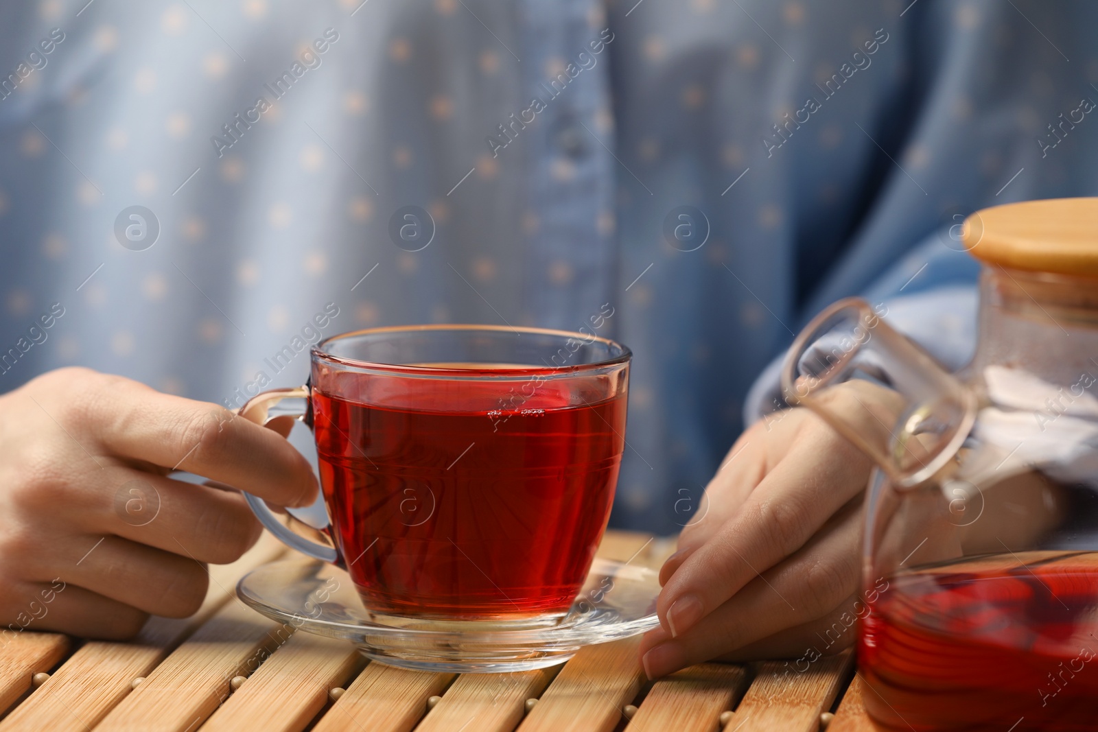 Photo of Woman with cup of delicious hibiscus tea at wooden table, closeup