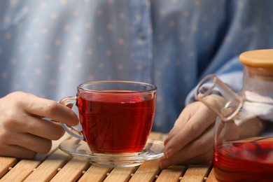 Photo of Woman with cup of delicious hibiscus tea at wooden table, closeup