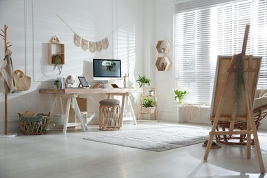 Stylish home office interior with comfortable workplace and easel