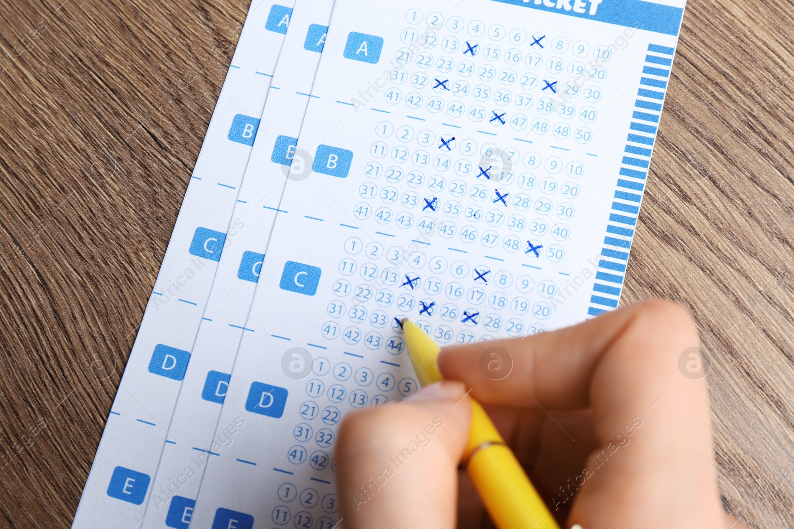 Photo of Woman filling out lottery tickets with pen on wooden table, closeup