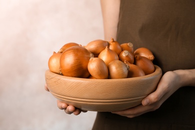 Photo of Woman holding bowl with ripe onions on grey background