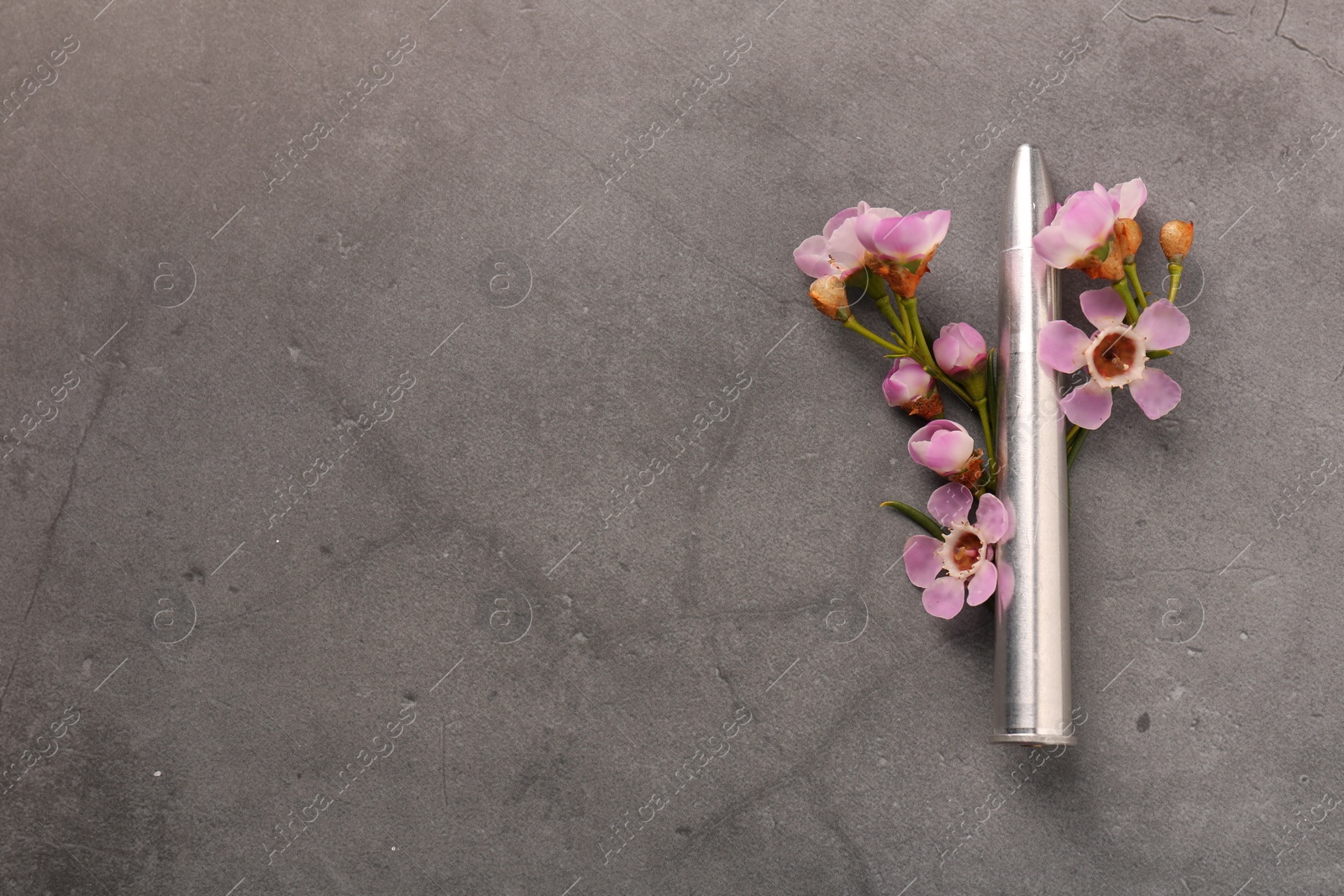 Photo of Bullet and beautiful flowers on grey textured table, flat lay. Space for text