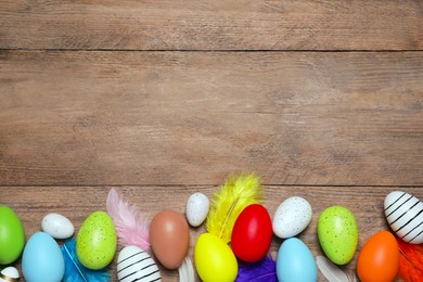 Photo of Flat lay composition with festively decorated Easter eggs and feathers on wooden table. Space for text