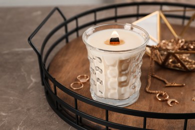 Photo of Burning soy candle with wooden wick near stylish accessories on grey table