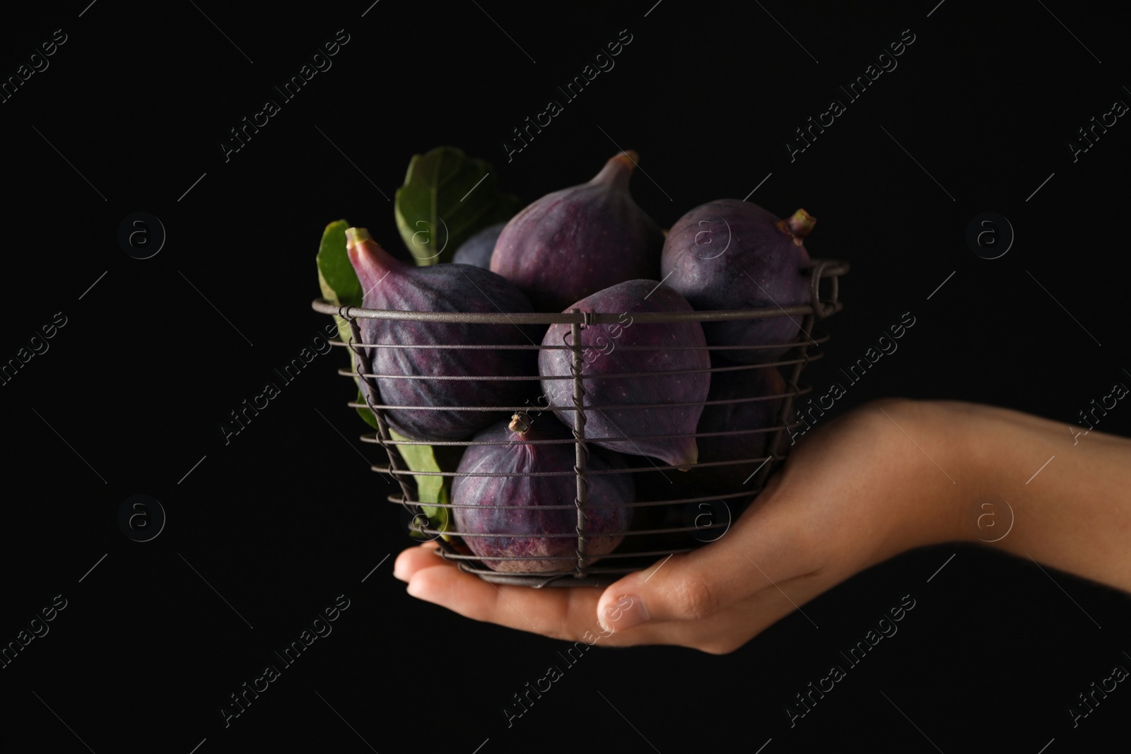 Photo of Woman holding basket with tasty raw figs on black background, closeup
