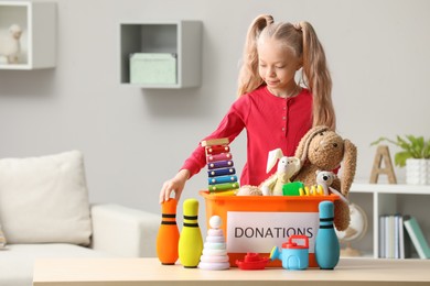 Photo of Cute little girl sorting donation box at home