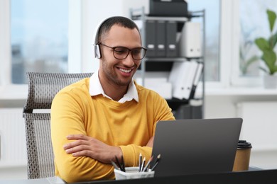 Young man with headphones working on laptop at table in office