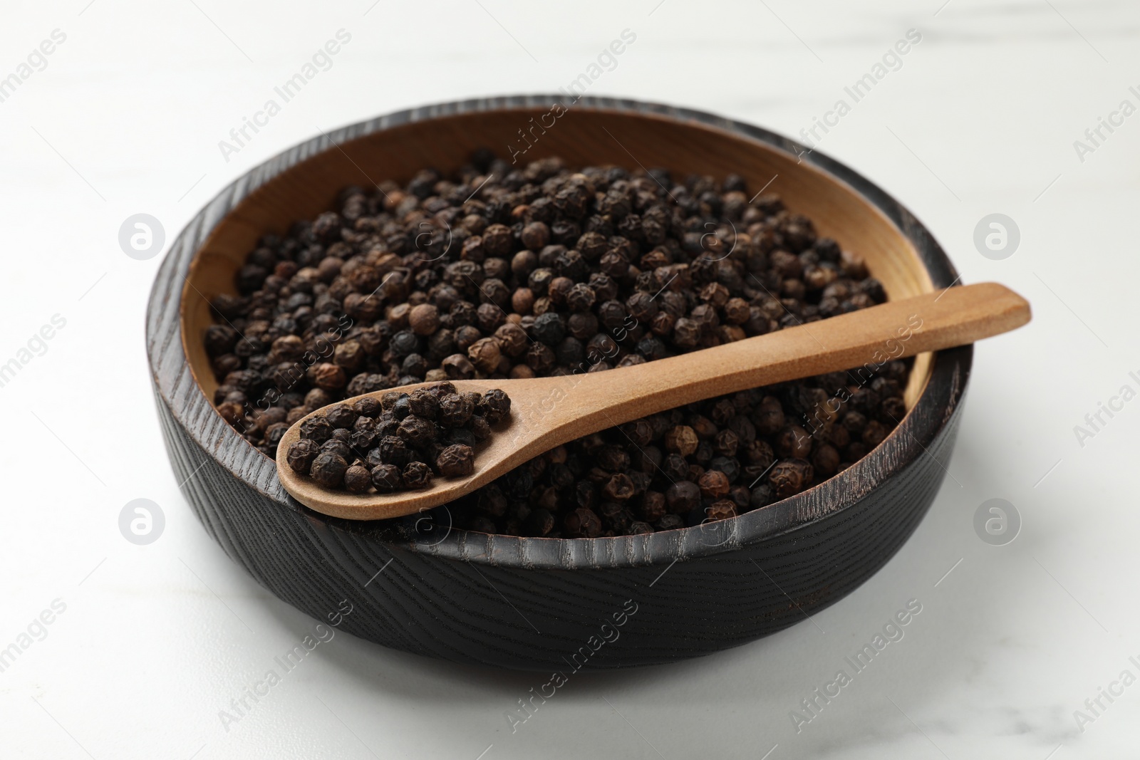 Photo of Aromatic spice. Black pepper in bowl and spoon on white table