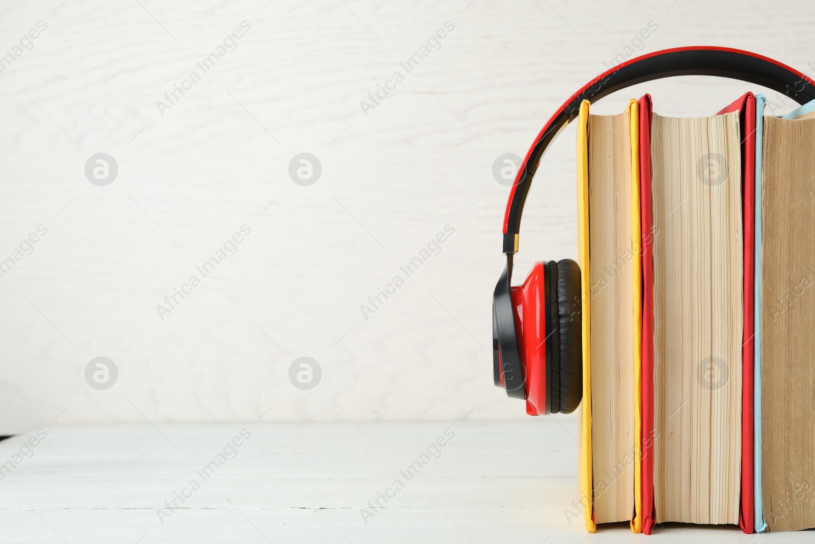 Photo of Books and modern headphones on white wooden table. Space for text