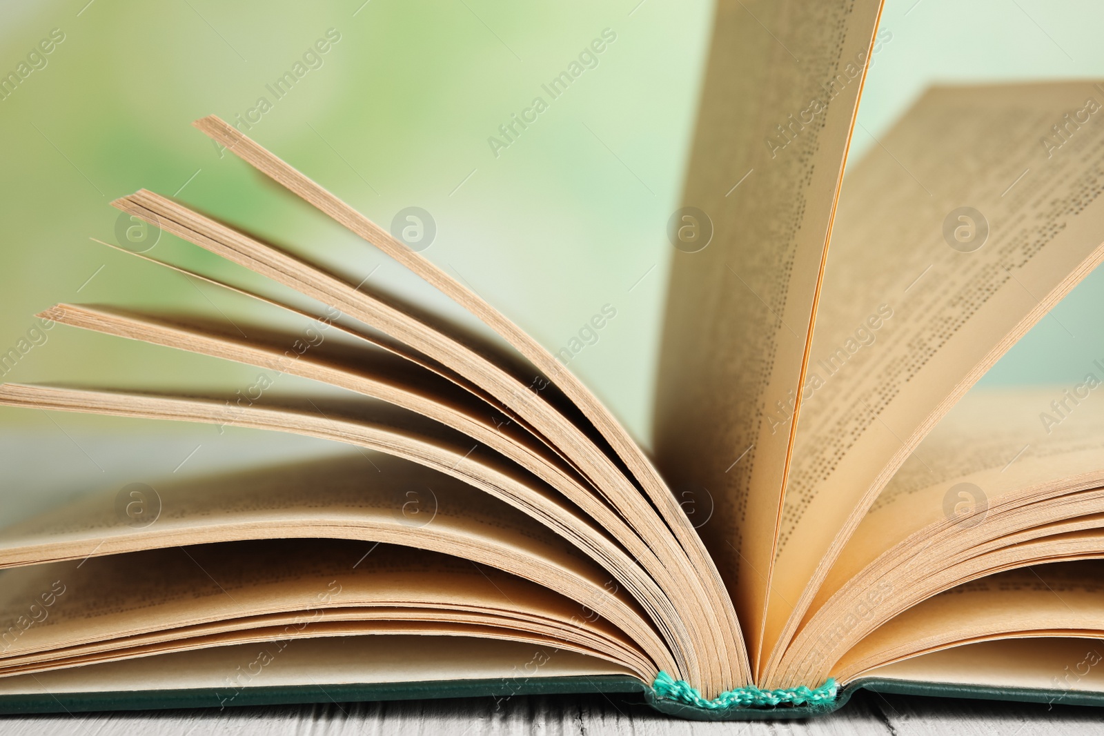 Photo of Open book on white wooden table against blurred green background, closeup