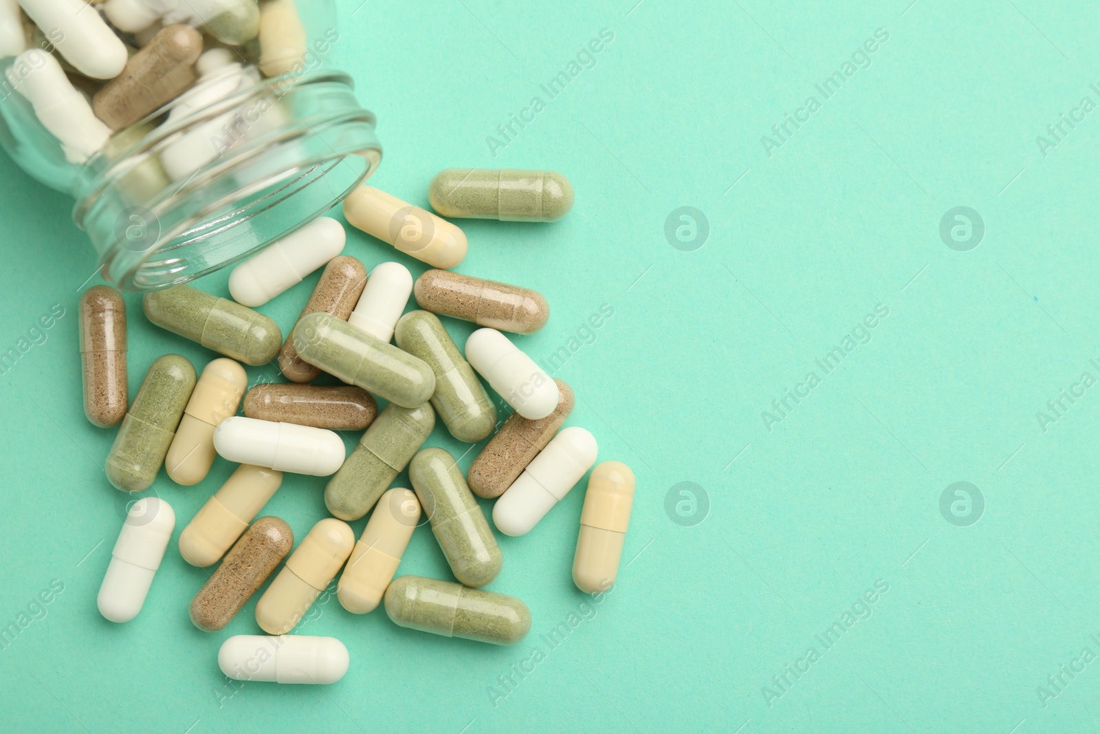 Photo of Vitamin pills and bottle on mint color background, top view. Space for text