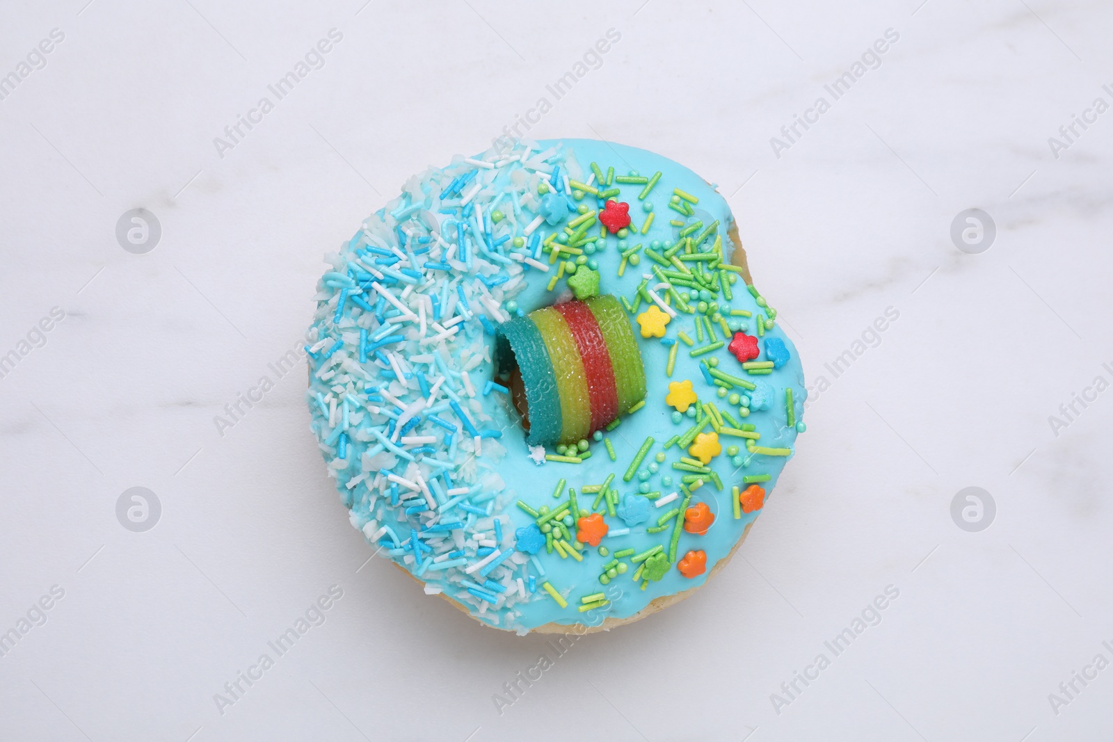 Photo of Sweet glazed donut decorated with sprinkles on white marble table, top view. Tasty confectionery