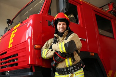 Firefighter in uniform near red fire truck at station, low angle view