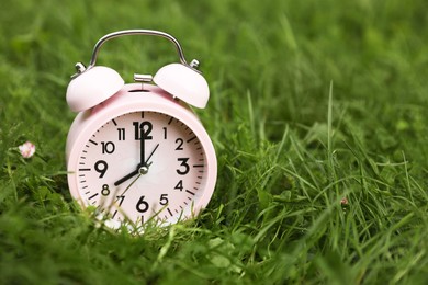 Photo of Pink alarm clock on green grass outdoors, space for text