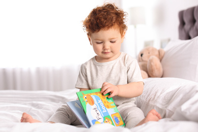 Cute little child playing with book on bed at home