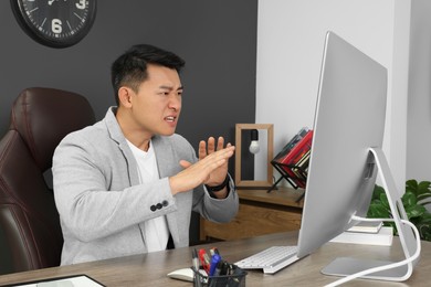 Emotional boss having online meeting via computer at wooden table in modern office