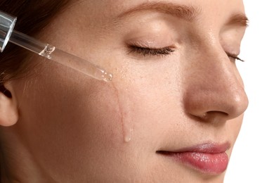 Photo of Beautiful woman with freckles applying cosmetic serum onto her face on white background, closeup