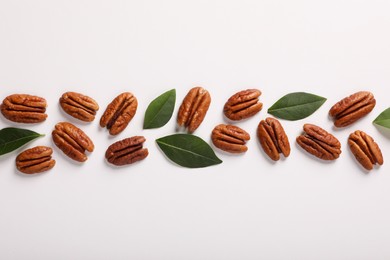 Delicious pecan nuts and green leaves on white background, flat lay