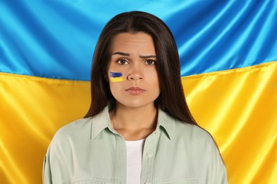Photo of Sad young woman with face paint near Ukrainian flag