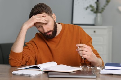 Photo of Overwhelmed man suffering from headache at table indoors