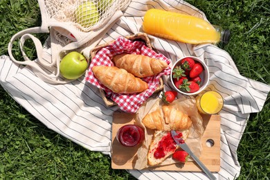 Photo of Blanket with different products on green grass, top view. Summer picnic