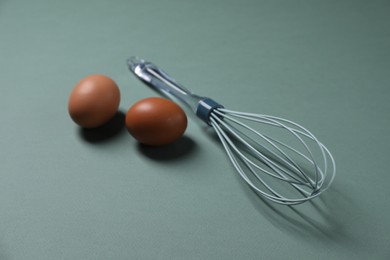 Photo of Whisk and raw eggs on pale blue background