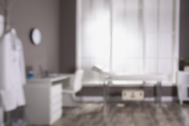 Photo of Blurred view of modern medical office with doctor's workplace and examination table. Interior design
