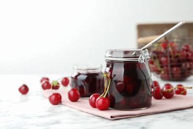 Photo of Jars of pickled cherries and fresh fruits on white marble table. Space for text