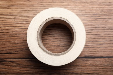 Photo of Roll of adhesive tape on wooden background, top view