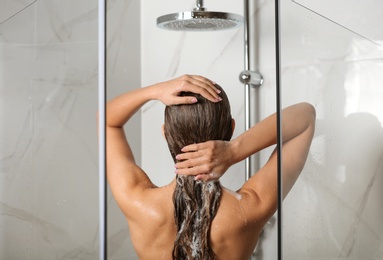 Image of Young woman washing hair in shower at home, back view