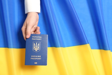 Woman holding Ukrainian travel passport over national flag, top view with space for text. International relationships