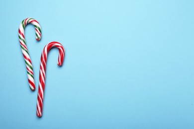 Photo of Two sweet Christmas candy canes on light blue background, flat lay. Space for text