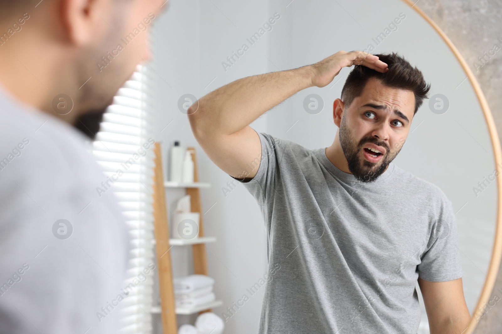 Photo of Emotional man examining his head near mirror in bathroom. Dandruff problem